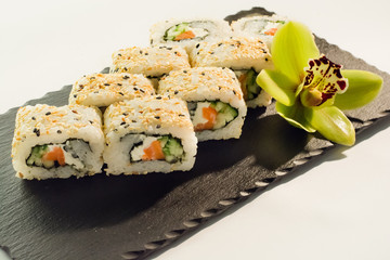 Salmon sushi roll - cucumber, rice, cheese philadelphia, black sesame on slate texture closeup