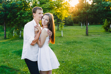 Loving man embraces his girl in a green area, sun in green trees on the back