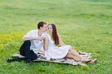 Boy and a girl in white drinking tea together sitting on a green grass