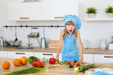 Pretty little girl in cook clothes opens his eyes and mouth on a kitchen