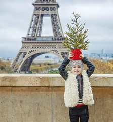 Fototapeta na wymiar child in front of Eiffel tower holding Christmas tree on head