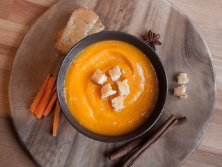 Pumpkin soup in a brown bowl on dark wood