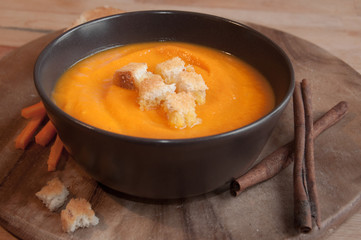 Pumpkin soup in a brown bowl on dark wood
