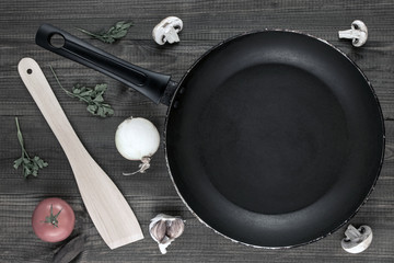 empty pan with mushrooms , tomato, garlic, onion, parsley leaves and wooden spatula on wooden table.