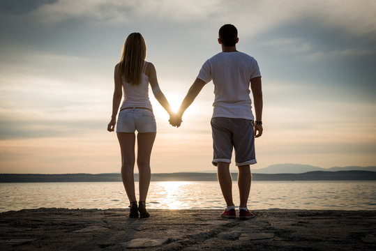 Young couple in love, silhouettes. Attractive man and woman enjoying romantic evening on the beach, Holding hands watching the sunset, valentine's, family concept