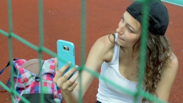 Girl sitting behind net and doing selfies on smartphone, steadycam shot
