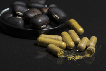 Pill capsule that contain herbal medicine powder of mucuna pruriens seed with blurred of velvet bean seed at the blackground, Mucuna pruriens seed have been used for traditional medicine, selective fo