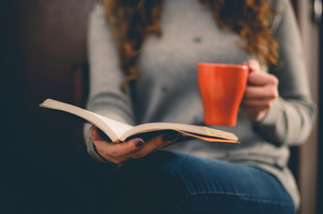 Ragazza si rilassa bevendo un the e leggendo un libro.
