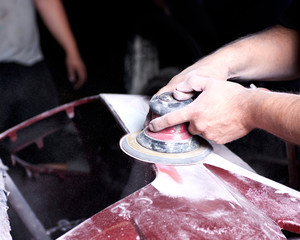 Worker is sanding filler with air sander in auto body shop
