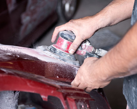 Worker is sanding filler with air sander in auto body shop