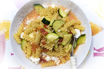 Top down view on single round plate of pasta with squash, tomato and cheese. Fork inside
