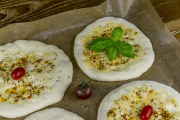Four round flat bread pieces over wax paper. Includes basil leaves and tomato
