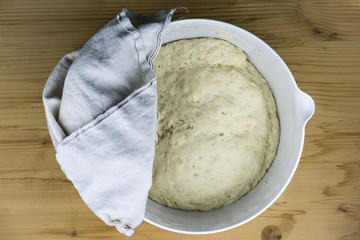 Top down view of bread batter rising in bowl. Cloth rag on top to cover it for enhancing the speed of yeast activation