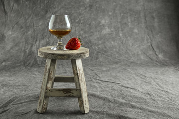 Brandy Snifter and Strawberry on a Mottled Grey Background on a small white stool