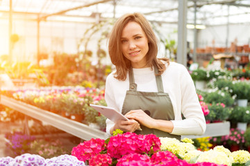 Young attractive woman working at the plants nursery using table