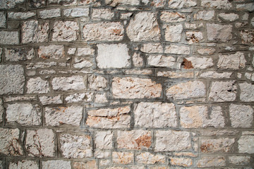 Texture of old cobblestone. Rocks of different sizes. City street. Some plant growing on the weathered wall.