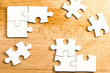 fill the gaps, white jigsaw/puzzle over a wooden table background, symbol of problem solving