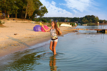 Dziewczynka puszcza bańki mydlane w jeziorze. - obrazy, fototapety, plakaty