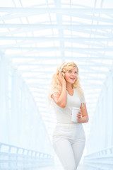 Morning rhythm / Beautiful young woman with music headphones, standing on the bridge with a take away coffee cup and posing against urban background.