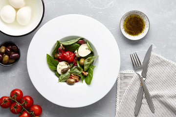 Italian salad with fresh basil leaves, olives, capers, walnuts, mozzarella cheese and red pepper on stone background.