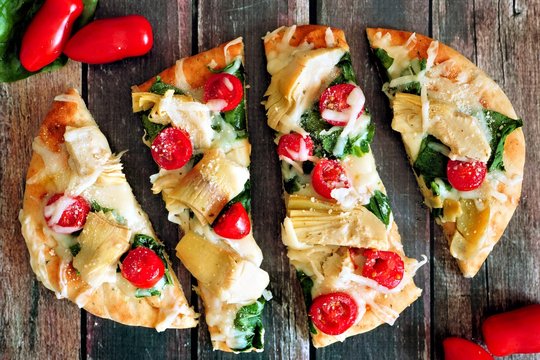 Flat bread pizza with melted mozzarella, tomatoes, spinach and artichokes, overhead view on rustic wood