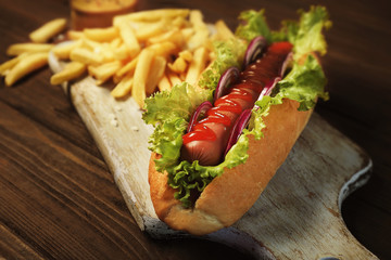 Delicious hot dog and fries on wooden board