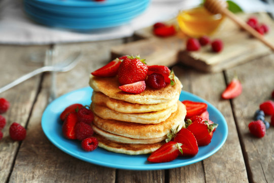 Tasty pancakes with fresh berries on plate on wooden background