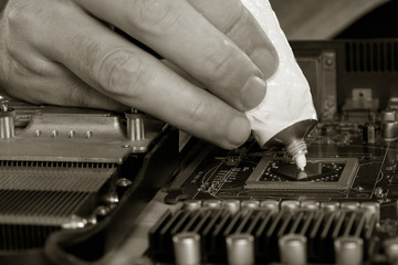 computer repair. black and white image men's fingers squeezed from a tube of thermal paste to the video processor. close-up selective focus