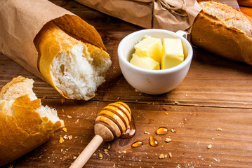 Breakfast is the traditional white baguette with butter and honey. On a wooden table, close view