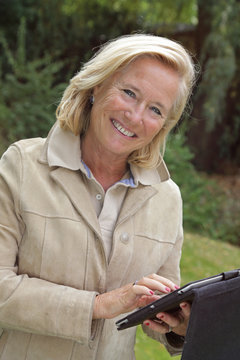 femme senior souriante tapant sur tablette dans jardin en automne