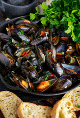 Boiled mussels in iron pan cooking dish. with herbs, butter, lime, parsley, garlic and fresh bread.