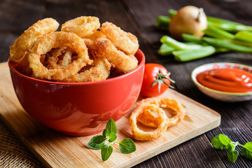 Deep - fried onion rings covered in breadcrumbs with ketchup
