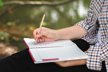 Close up of happy woman taking notes into notebook using pencil at a park