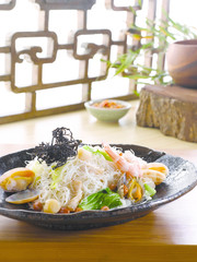 Fried shrimp and clams with rice vermicelli, lettuce on black pl