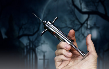Hand holds large needle in front of a graveyard background