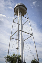 vertical image of a very tall water tower against a bright blue sky.