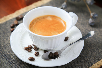 Hot milky cup of coffee with black bean around on the table
