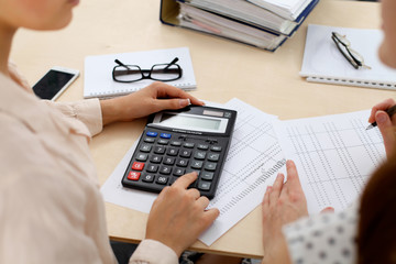 Two female accountants counting on calculator income for tax form completion hands closeup. Internal Revenue Service inspector checking financial document. Planning budget, audit  concept