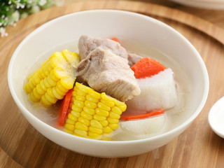 Corn and carrots yam stew with pork ribs in white bowl on wooden