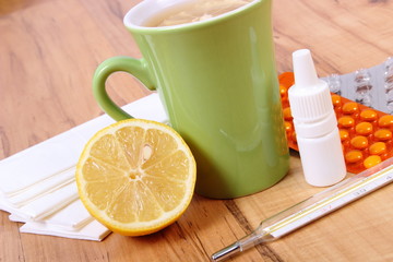 Pills and nose drops for colds, handkerchiefs and hot tea with lemon