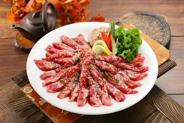 Seasoned sliced beef on white plate with lemon, mushroom and sal
