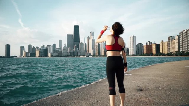 Runner athlete looking at skyscrapers and drinking water