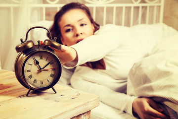 Woman in bed turning off alarm clock