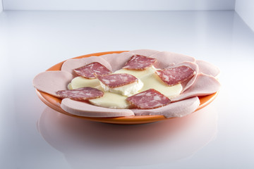 Мясная нарезка с моцареллой на оранжевой тарелке на светлом фоне