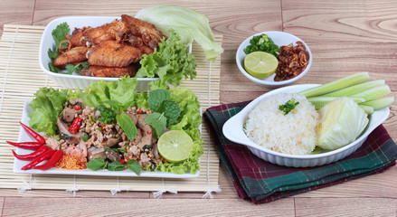 Sticky rice served with fried chicken and  spicy sour mixed herb salad of chicken and liver chicken on wood.   Top view.