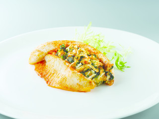 Fried stuffed tilapia with lettuce on white plate in restaurant