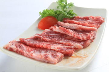 Sliced fresh raw beef on white plate with tomato and herbs