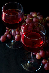 Two glasses of homemade rose wine and grapes on black wooden table. Low key