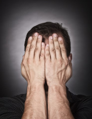 Studio portrait of a stressed Caucasian man covering his face with the hands