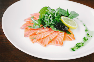 Stir fried sliced salmon with olive, lemon and herbs on white pl